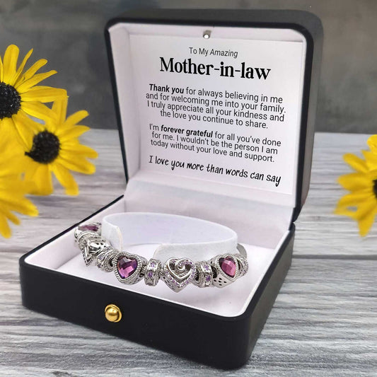 Bracelet with purple heart charms in a box with a message for a mother-in-law, surrounded by yellow flowers.