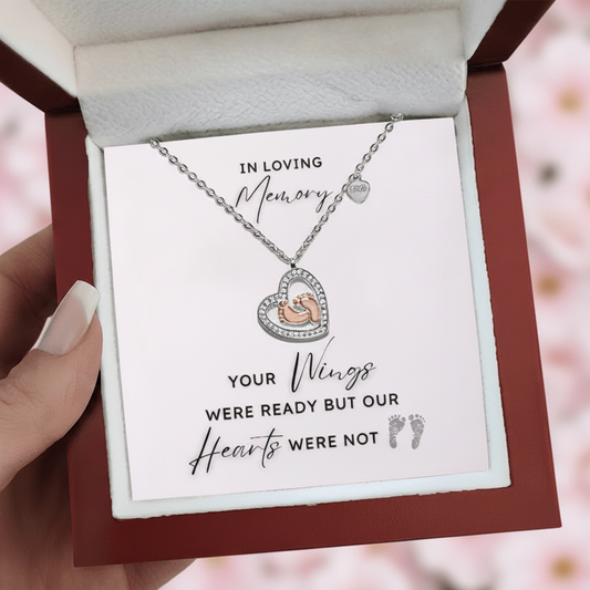 Necklace with a heart shape pendant with rose gold baby feet inside in a jewelry box with a message card.