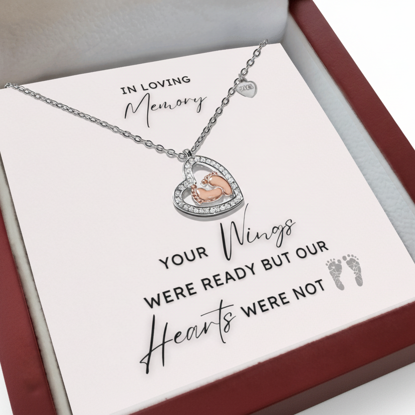 Necklace with a heart shape pendant with rose gold baby feet inside in a jewelry box with a message card.