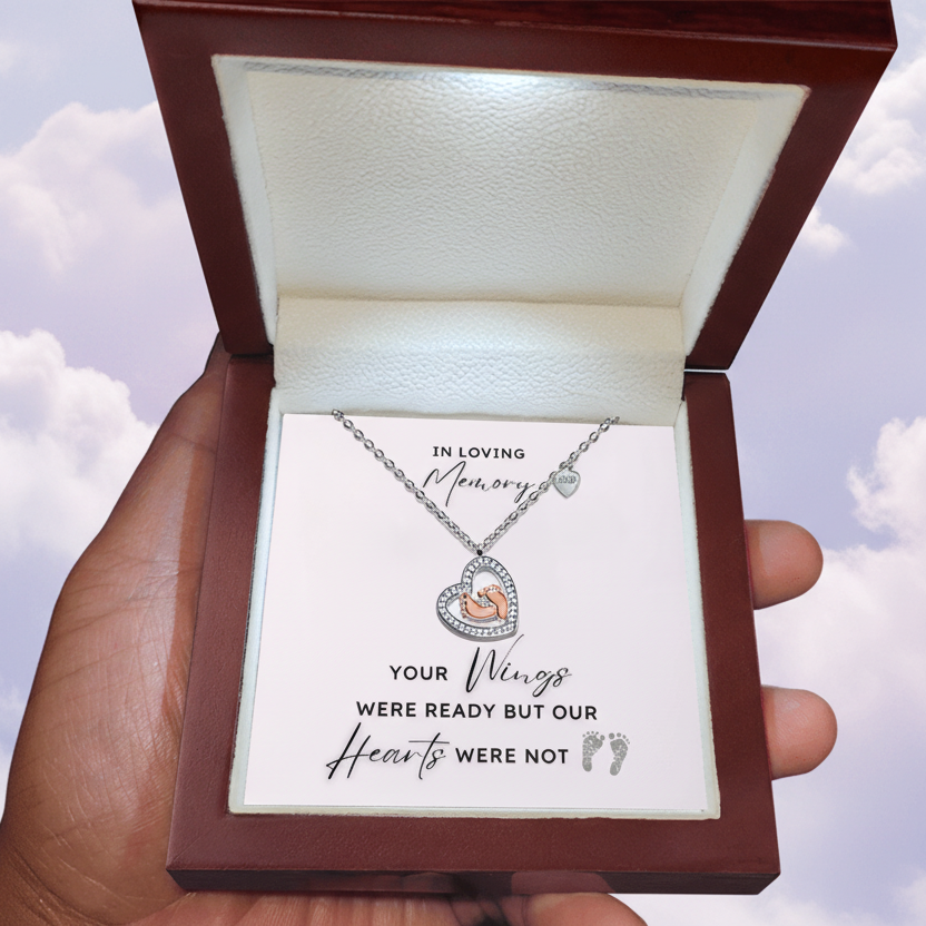 Necklace with a heart shape pendant with rose gold baby feet inside in a jewelry box with a message card.