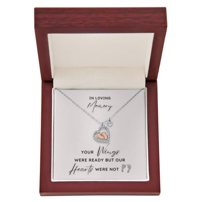 Necklace with a heart shape pendant with rose gold baby feet inside in a jewelry box with a message card.